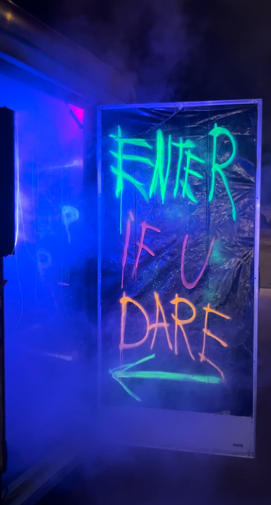 Neon sign with 'Enter if you dare' text in a dark, smoky setting